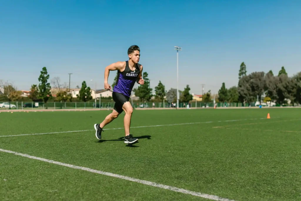 Atleta jovem correndo na pista de atletismo ao ar livre, praticando treino de velocidade em um dia ensolarado.