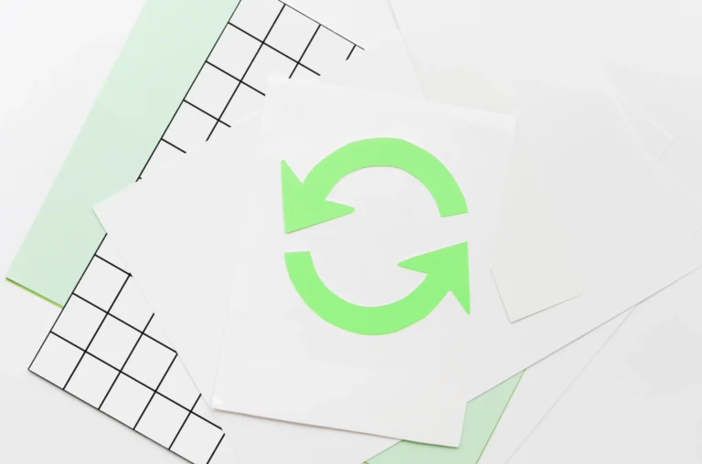 Imagem de cartões de reciclagem com símbolo de recursão em verde, simbolizando sustentabilidade e gestão de resíduos, sobre uma superfície com gráficos e papel.