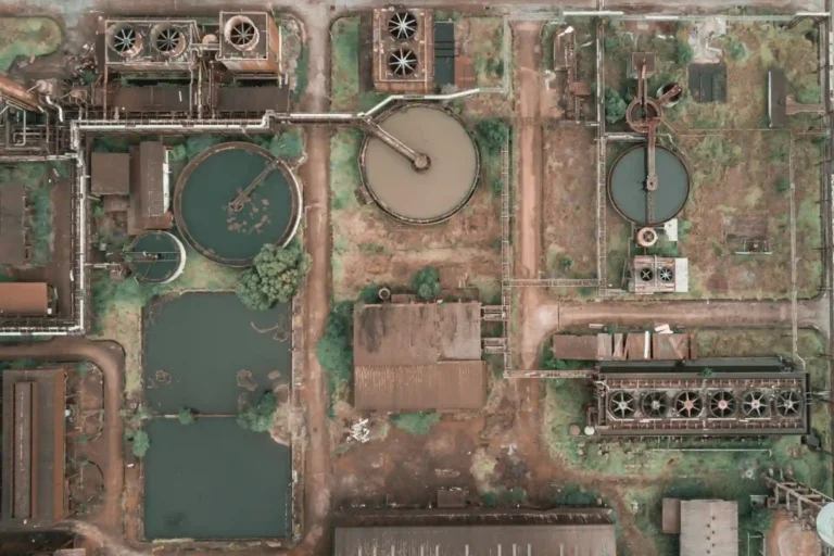 Imagem aérea de uma estação de tratamento de água com tanques, estruturas metálicas e áreas verdes, mostrando o funcionamento de uma planta de saneamento.
