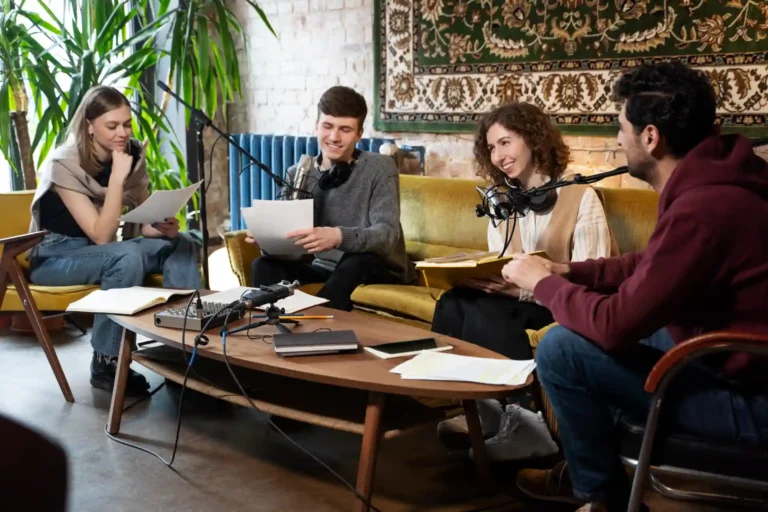 Grupo de pessoas participando de um podcast ao vivo em ambiente descontraído com microfones e livros, em um espaço com parede de tijolos e decoração moderna.